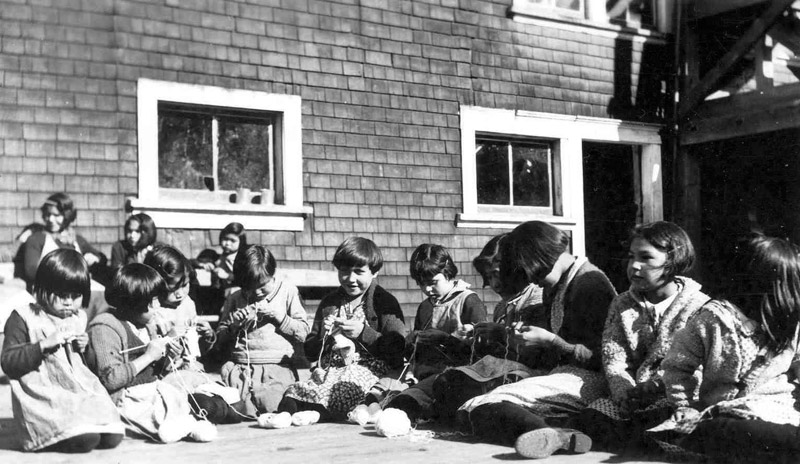 A class sitting outside and knitting.