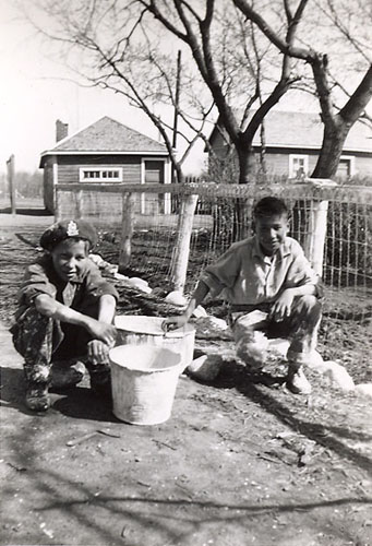 Two boys who have finished whitewashing a fence, File Hills Indian Residential School.