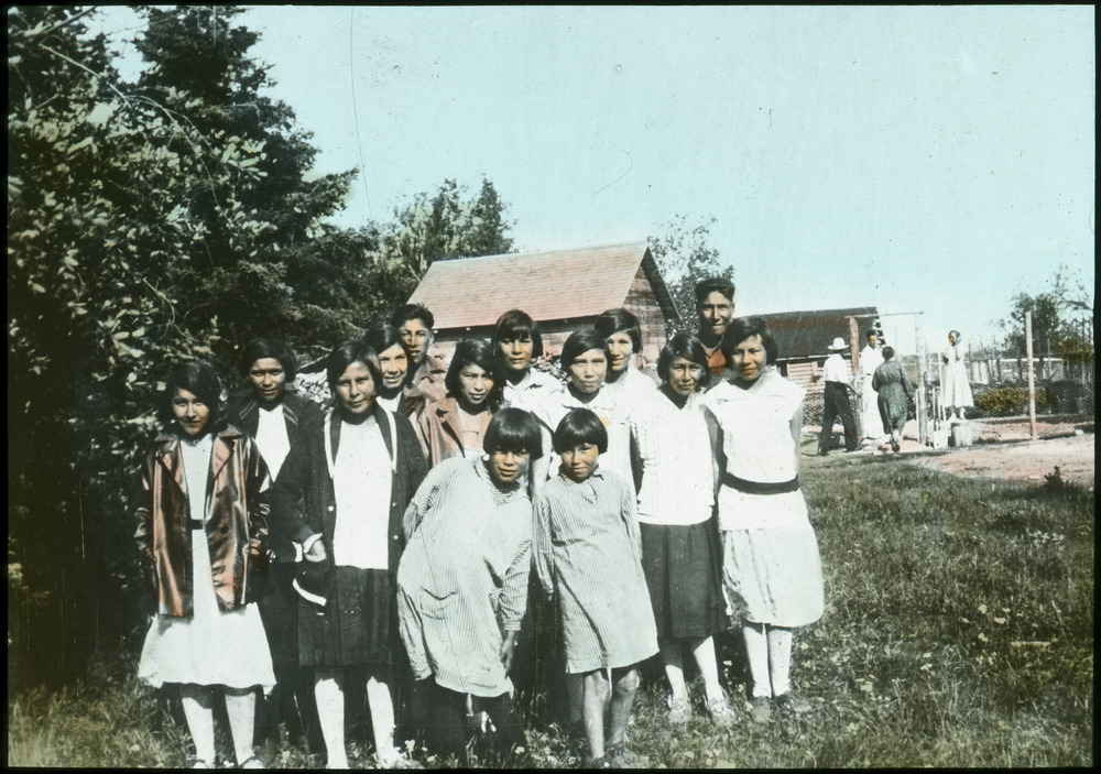 Group of youth posing outside, buildings and trees in the background.