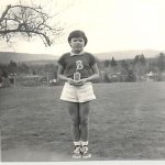 Photo of a youth in a soccer uniform standing outdoors with a trophy.