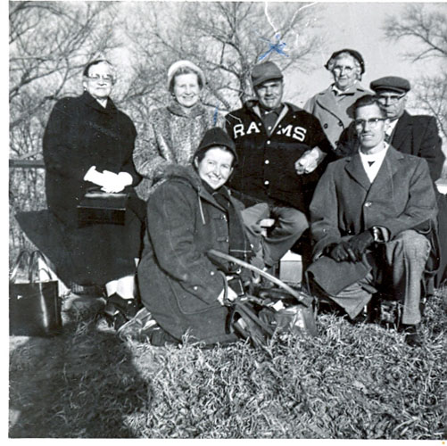 Staff group, they are wearing hats and jackets, shadow of the photographer in the shot