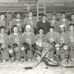 Portrait of youth in hockey gear and team uniforms with one person in a suit standing in the centre.