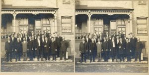 Group portrait of people wearing suits, standing in front of building.