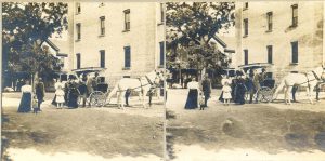 People standing with horse and carriage in foreground building seen in the background.