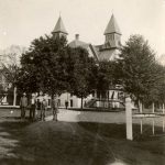 Children standing in the front left foreground, with the building and trees seen in the background.