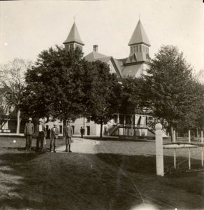 Children standing in the front left foreground, with the building and trees seen in the background.