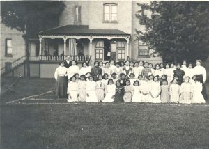 Staff and children seated and standing posed for a photograph, outdoors in front of Mount Elgin Residential School.