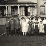 Some younger children and a staff member standing posed for a photograph in front of Mount Elgin Residential School