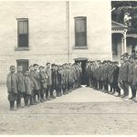 Children standing in two lines forming a V, outdoors in front of Mount Elgin Residential School