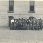 Children and staff seated and standing posed for a photograph, outside in front of Mount Elgin Residential School