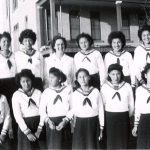 Group of 12 youth in Canadian Girls in Training uniforms, standing posed for a photograph in front of File Hills Residential School.