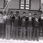 Group of thirteen youth standing posed for a photograph on the steps of File Hills Residential School.