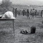 Group of youth and Mrs. Card standing in a circle outdoors in the background and a table with lunch on it, cart and bucket in the foreground.