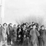 Group of children and youth standing and seated posed for a photograph outside of Round Lake Residential School in winter.