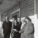 Group of six staff members on a porch, standing posed for a photograph up against a building.