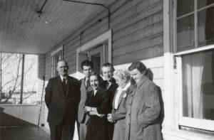 Group of six staff members on a porch, standing posed for a photograph up against a building.