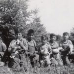 A group of six children kneeling and holding ducks in front of trees.