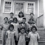 Group of ten children standing posed for a photo on the front steps of Round Lake Residential School.