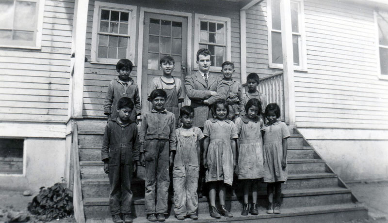 Black and white photo of children with a teacher on the steps of Round Lake residential school