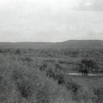 View of the road leading from Round Lake Residential School, including forest and fields, Qu'Appelle Hills and smoke coming up in the background.