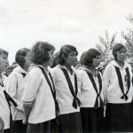 Choir leader conducting in front of a group of children in uniform singing