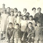 Group shot of reverend and youth on grounds of Norway House Residential School with school in background.