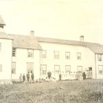 Children and staff in front of Norway House Residential School buildng from a distance.