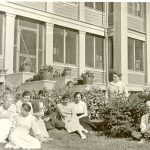 Staff sitting and standing near Norway House Residential School building.