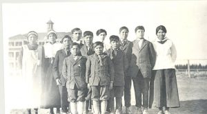 Group shot of reverend and children in front of school building.