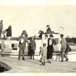 Candid image of people who went on a fishing trip. They are standing, some are on the dock and some are on the boat. Most are facing the camera.