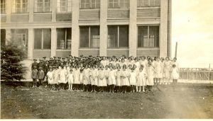 Children standing for a group photograph in front of the Norway House Residential School building. Students appear to be wearing uniforms.