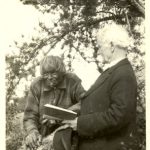 The reverend reading to John Meneno. Both people are standing outdoors.