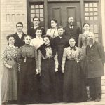 Twelve staff members posed in front of large door, caption reads 