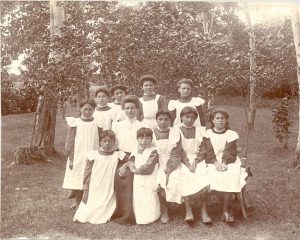 Ten children in aprons posed around a staff member in yard