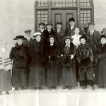 Formal portrait of the staff of Brandon Residential School, standing on some steps.