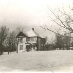 Image of a house on a property on a slight hill, some trees surrounding it, taken in winter.