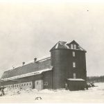 Dairy barns and silos, with tree line in background.