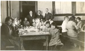 [Principal Ferrier and two staff members supervising students in the dining hall at dinner time, Brandon Institute]