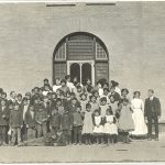 Group portrait of children and staff of Brandon Residential School, standing in front of the school.