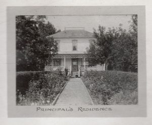 Principal's Residence in the background with path leading up to it, lined with shrubs, caption reads 