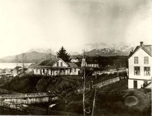 Partial view of Crosby Boys' Home on the right with the mission house at centre of image, mountains and ocean in the background.