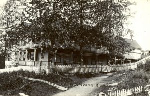 Hospital with large tree in front, surrounded by picket fence and path leading up to it.