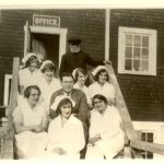Dr. Large with nurses in uniform seated on some steps leading up to a door, with a sign reading 