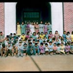 Large group of children posing in front of Brandon Industrial School, hand coloured