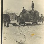 Rev. Charles Hopkins and another person on freight sleigh, lead by horses in the winter. School in the background.