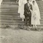 Wedding party standing on stairs. The bride and groom are seen on the bottom step in front, the rest of the party is lined up behind them in pairings and small groups on the higher steps.