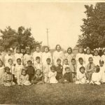 Children in a group, front row is seated on the grass, middle row is kneeling with back row standing.