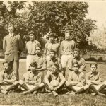 Eleven football players, wearing their team uniforms. Some seated, some kneeling some standing. Coach is standing next to the back row.