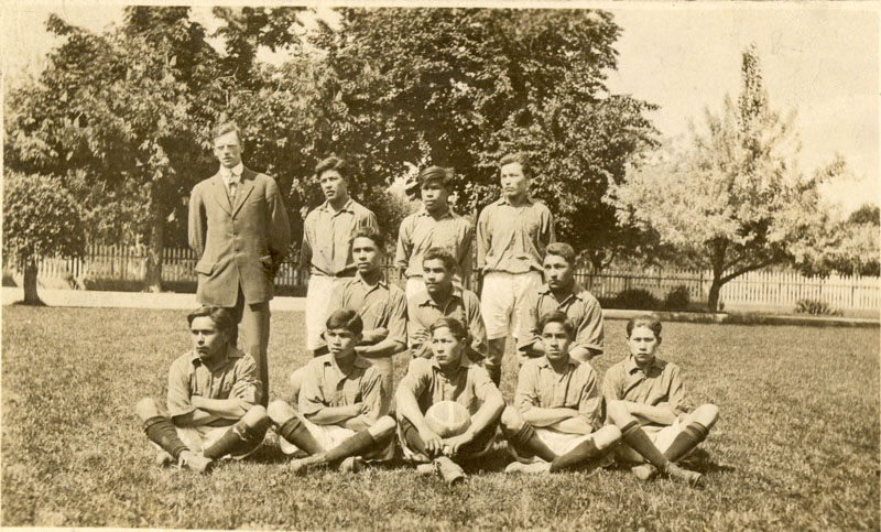 Eleven football players, wearing their team uniforms. Some seated, some kneeling some standing. Coach is standing next to the back row.