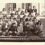 Large group of children and staff seated and standing posed for a portrait on the steps of Kitimaat Residential School.